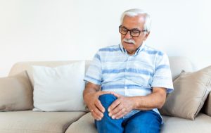 gambar seorang pria lanjut usia sedang nyeri lutut memakai baju garis biru. Gambar ini dipakai untuk artikel Klinik Utama Dr. Indrajana membahas tentang pengapuran tulang.