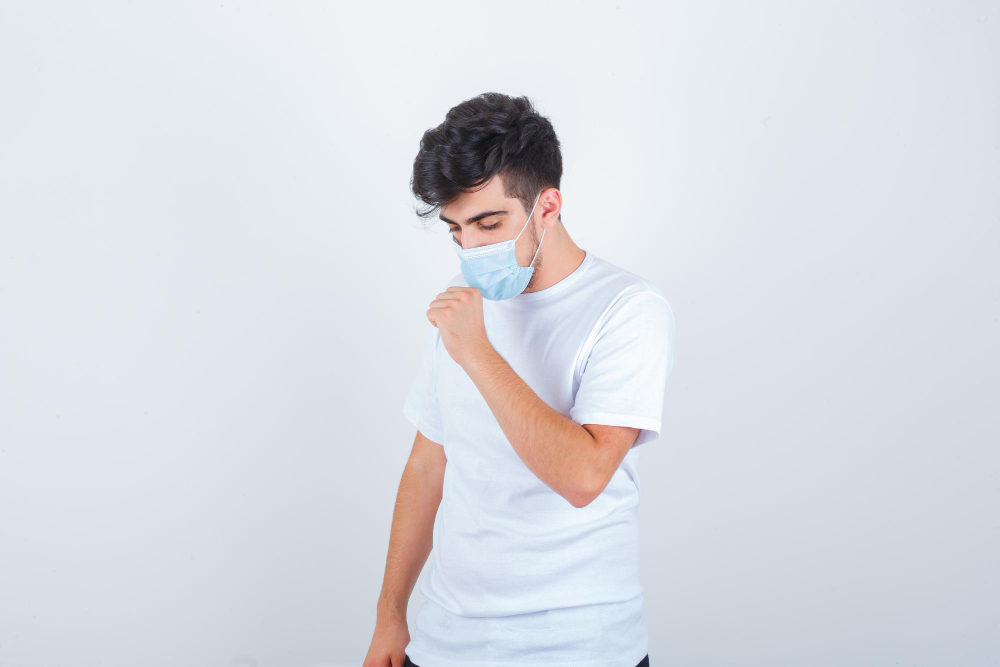 seorang pria sedang mengalami batuk. Dia memakai masker sebagai salah satu etika batuk dan bersin untuk artikel Klinik Utama DR Indrajana, ditulis oleh Jeremi Napoli Siregar.