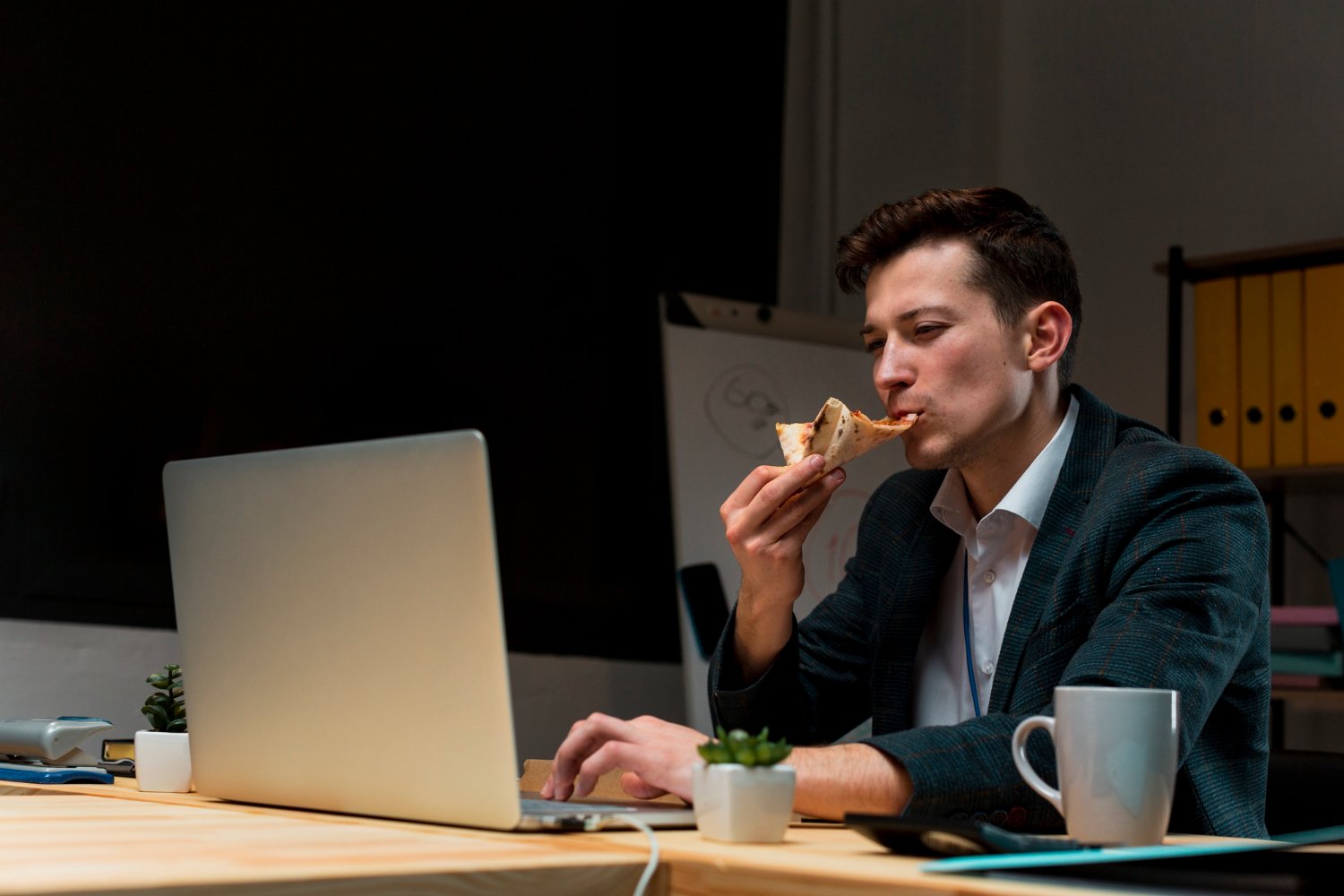 gambaran pria sedang makan pizza di kantor saat sedang bekerja - section image untuk artikel bagian fakta diabetes early onset di Indonesia. Ditulis oleh Jeremi Napoli Siregar di Klinik Utama DR. Indrajana.